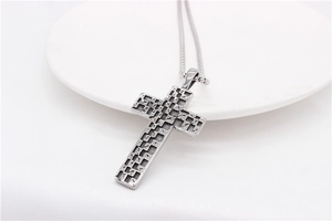 Detailed view of silver mosaic cross pendant with textured finish on white ceramic