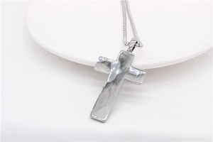 Close-up of silver cross pendant with hammered metal texture on white ceramic plate