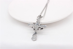 Detailed view of silver gothic cross pendant with rose motif on white ceramic plate