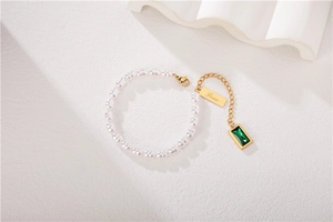 Macro detail of pearl bracelet with emerald green gemstone and Love engraved gold charm