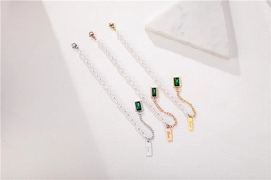Macro view of emerald green stone necklaces with Love pendant in gold, silver, and rose gold