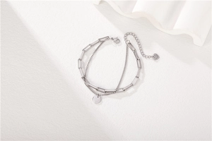 Detail eines silbernen zweilagigen Titanstahl-Armbands mit rundem Anhänger und Herz