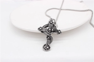 Detail of vintage steel dragon cross necklace with skull relief on white ceramic