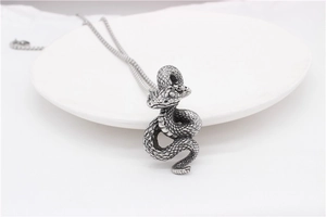 Macro shot of silver snake pendant with detailed scales on a white porcelain dish