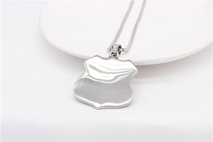 Macro view of polished silver shield pendant and bead chain on a ceramic plate