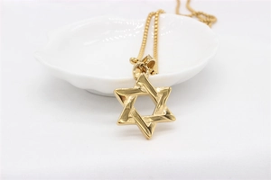 Close-up of polished gold Hexagram pendant on a delicate box chain against white decor