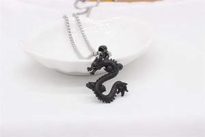 Close-up of a black dragon pendant on a silver chain inside a white seashell tray