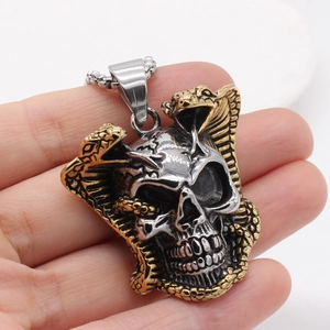 Punk style snake and skull pendant in silver and gold, held in hand to show scale
