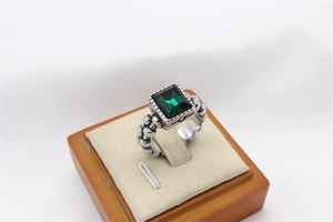 Macro detail of retro silver ring with emerald cut green stone and beaded texture