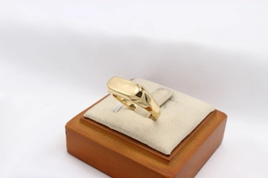 Détail macro d'une bague chevalière rectangulaire dorée polie sur un support en bois