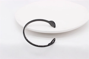 Detailed view of a sleek black minimalist open cuff bracelet on white ceramic plate