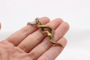 Detail of gold snake pendant with textured scales and silver box chain held in hand