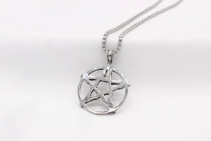 Gros plan d'un pendentif pentagramme en argent vintage avec chaîne box sur tissu blanc