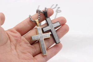Détail de pendentifs croix vintage en acier titane tenus à la main en noir et or