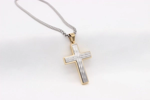 Vue macro d'un pendentif croix bicolore avec texture diamantée fine et chaîne box argentée