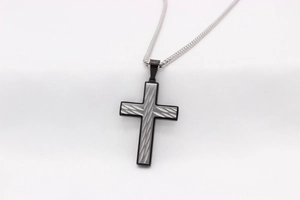 Vue macro du pendentif croix en acier brossé avec bordure noire et chaîne métallique
