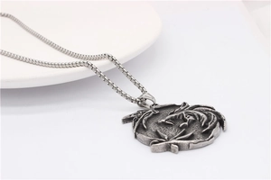 Macro view of vintage silver dragon relief pendant on a box chain in a white ceramic dish