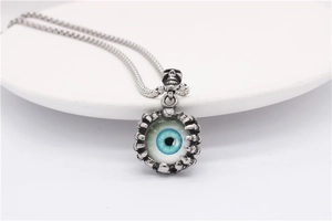 Detail of gothic devil eye pendant with skeletal claw and blue eye on steel chain