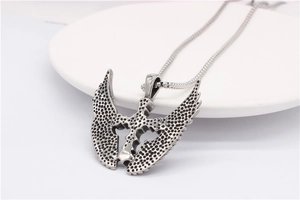 Close-up of retro stainless steel fallen angel wing pendant with cross detail on white dish