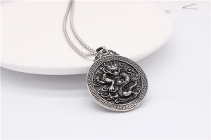 Detail of vintage silver dragon relief pendant with intricate cloud patterns and woven chain