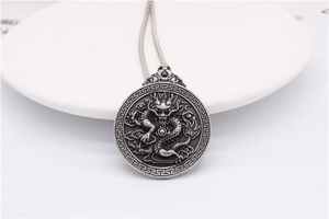 Macro detail of silver dragon relief on round titanium steel pendant with vintage pattern