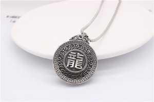 Detail of round silver pendant featuring embossed dragon character and cloud patterns