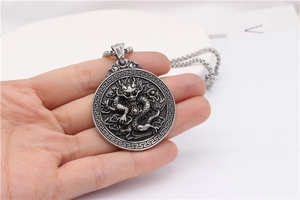 Detailed view of hand holding a round stainless steel necklace with Chinese dragon relief