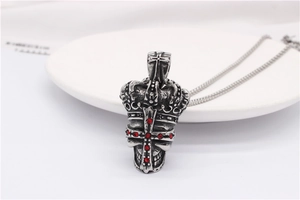 Vue détaillée du pendentif croix couronne gothique avec gemmes rouges sur chaîne acier