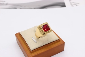 Detailed close-up of a gold-finish ring featuring a red square gem and Greek Key motifs