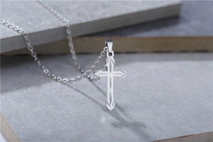 Macro shot of silver cross pendant with diamond-cut texture on grey stone background