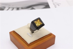 Macro shot of a black ring featuring a square yellow gemstone and geometric engraving