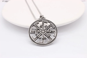 Détail d'un pendentif viking vintage avec roue solaire Kolovrat ajourée sur socle blanc