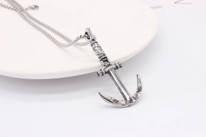 Macro shot of vintage anchor pendant on a white ceramic plate with silver steel chain