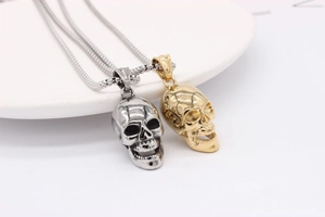 Detail of silver and gold skull pendants on round snake chains over white ceramic