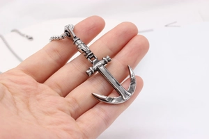 Close-up of a vintage silver anchor pendant on a bead chain held by hand for size