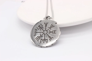 Detail of vintage silver Viking Vegvisir compass pendant on a white ceramic plate