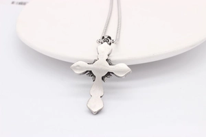 Detail shot of vintage stainless steel cross pendant with retro brushed finish on white plate