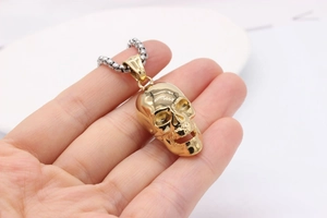 Detail of a vintage golden skull pendant with a silver wheat chain held by a hand
