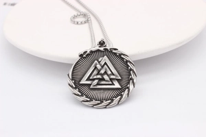 Detailed view of vintage silver steel Viking Valknut pendant on a white ceramic plate