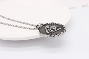 Detailed close-up of retro silver Valknut Viking pendant on a white ceramic surface