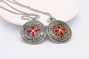 Macro detail of round shield pendant with red enamel cross and Latin engraving decor