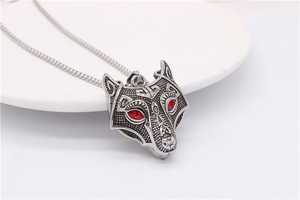 Close-up of vintage silver wolf head pendant with red gemstone eyes and Nordic patterns