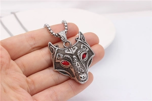 Close-up of vintage wolf head pendant with red gemstone eyes held in hand