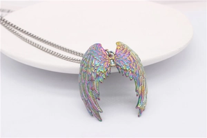 Detail of a rainbow-plated angel wing pendant with intricate feather carvings on a tray
