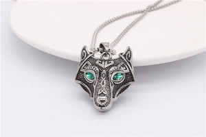 Detailed relief of a silver wolf head pendant with green gem eyes on a bead chain