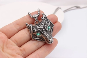 Detail of silver wolf head pendant with green gem eyes and vintage engraving