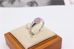 Dettaglio di un anello a sigillo d'argento con gemma rosa su un supporto di velluto beige