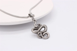 Close-up of vintage silver snake pendant with detailed scales on white ceramic tray
