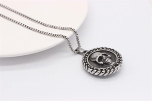 Detailed view of vintage skull pendant on a silver box chain over a white ceramic plate