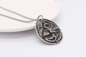 Detail of vintage embossed dragon pendant with bead chain on white plate surface